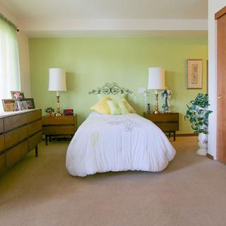 A cozy vintage-style bedroom with a green accent wall, featuring a bed with white bedding flanked by two wooden side tables and lamps.