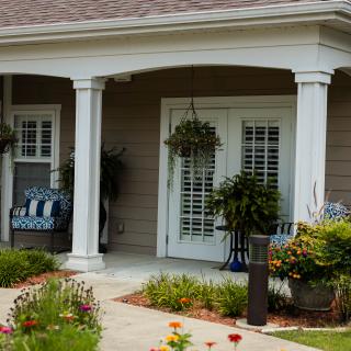A cozy porch with columns, decorated with hanging plants and outdoor seating.