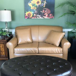 A cozy living room setting featuring a leather couch, an ottoman, and a vibrant piece of artwork.