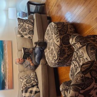 A man relaxing and reading a book on a patterned couch in a cozy living room.
