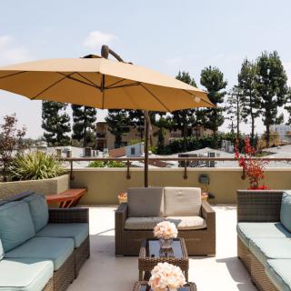 A comfortable outdoor patio with cushioned seating and a large umbrella, surrounded by greenery.