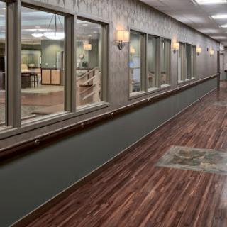A well-lit hallway featuring wooden flooring and large windows, typical of a commercial or healthcare environment.