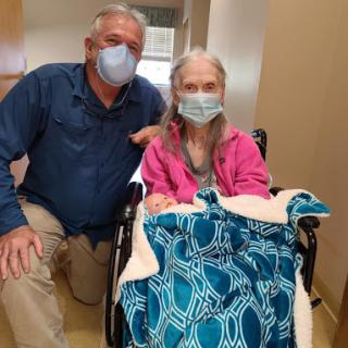 A caregiver and an elderly person pose together in a hospital setting, both wearing masks.