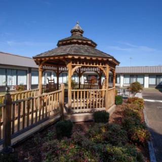 A wooden gazebo situated in a landscaped courtyard surrounded by a building on a clear day.