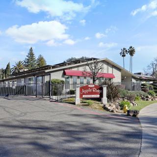 The exterior view of a motel with a driveway and surrounding trees under a blue sky.