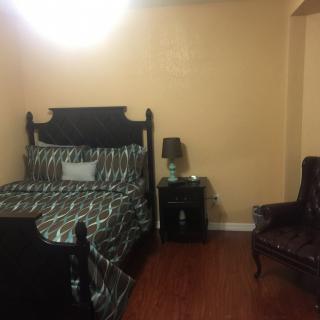 A cozy bedroom with a bed, side table, lamp, and armchair.