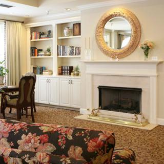 A cozy living room with a floral sofa, bookshelves, and a fireplace adorned with a circular mirror.