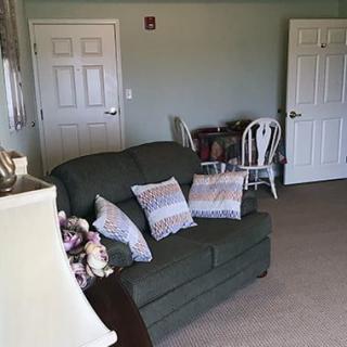 A cozy living room with a green sofa and decorative pillows, two chairs by the wall, and closed doors.