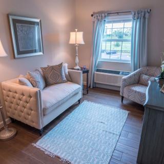 A cozy living room with elegant furniture, including a tufted sofa and armchair, illuminated by lamps beside a window.
