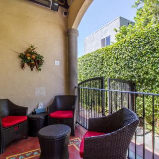 A cozy outdoor patio with wicker chairs and a small table, surrounded by greenery.