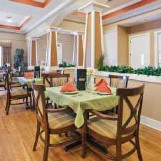 A neatly arranged restaurant dining area with tables and chairs, featuring green tablecloths and orange napkins.