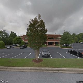 A cloudy day view of a parking lot in front of a building, with several cars parked and trees surrounding the area.