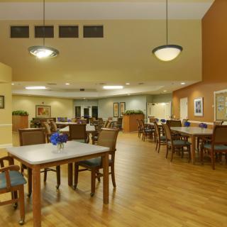 A spacious dining room with multiple tables and chairs, featuring warm lighting and a wooden floor.