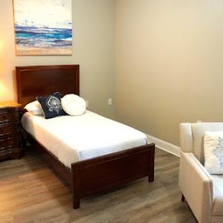 A cozy and minimalist bedroom setup featuring a single bed, a chair, and decorative artwork on the wall.