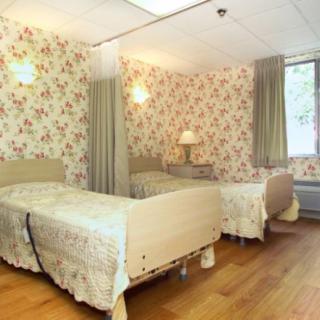 A shared nursing home bedroom with floral wallpaper and cozy beds.