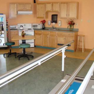 A rehabilitation room featuring parallel bars and a kitchen setup for therapy exercises.