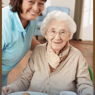 A caregiver and an elderly woman share a happy moment during mealtime in a nursing home.