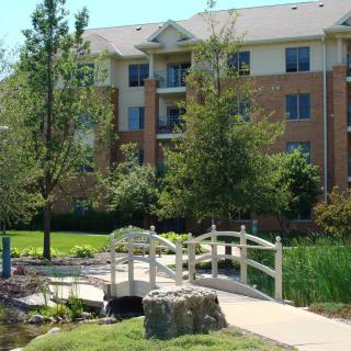 A scenic view of an apartment complex with a small bridge and lush landscaping.