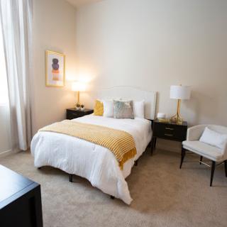 A well-lit, cozy bedroom featuring a comfortable bed with soft linens and stylish decor.
