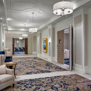A luxurious hallway with elegant furniture, ornate carpet, and chandeliers.