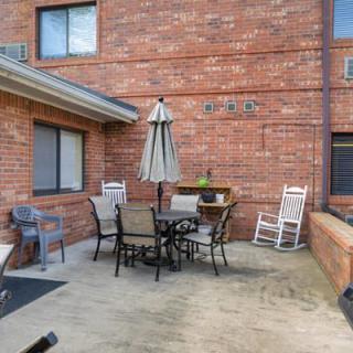 A cozy patio with outdoor furniture, including a table, chairs, and an umbrella against a brick wall.