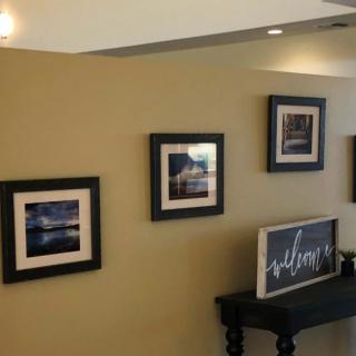 A cozy interior wall displays framed pictures and a welcoming sign on a small table.