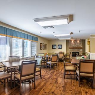 A cozy dining room with multiple tables and chairs, featuring a wooden floor and large windows.