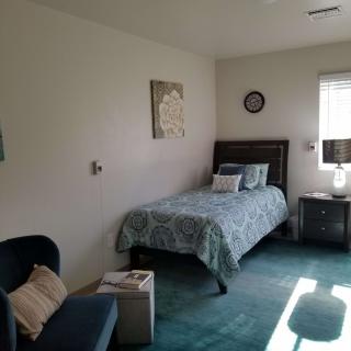 A cozy bedroom with a single bed, nightstand, and chair next to a window.