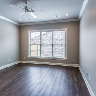 A bright, empty room with hardwood floors, a ceiling fan, and a large window.