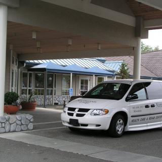 A white van parked under a covered entrance of a building with potted plants nearby.