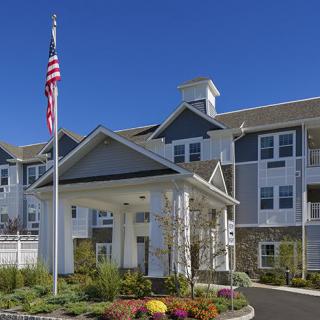 A modern residential apartment building with landscaped surroundings and a flagpole at the entrance.