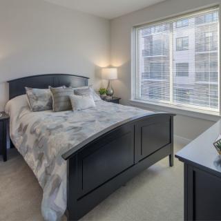 A cozy bedroom with a bed, lamps, and a large window allowing natural light.