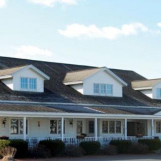 A large white house with dormer windows and a spacious porch under a clear blue sky.