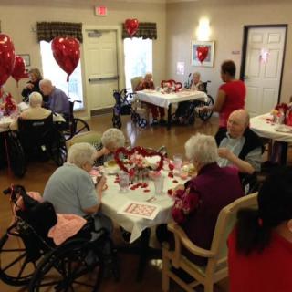 Elderly residents celebrating Valentine's Day in a nursing home with festive decorations and heart-shaped balloons.