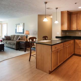 An open concept kitchen and living room with wood cabinetry and pendant lighting.