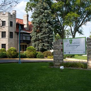 A historic castle-like building with a well-maintained garden and a sign in the foreground.