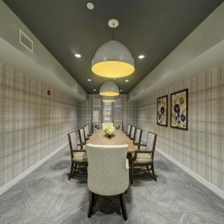 A modern dining or conference room featuring a long table with chairs and decorative pendant lighting.
