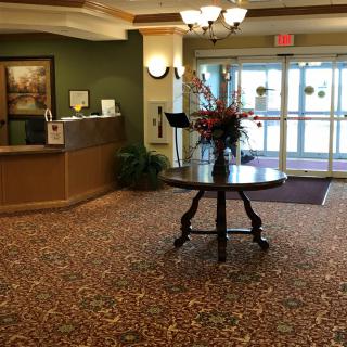 A hotel lobby with a reception desk, floral centerpiece, and entrance doors.
