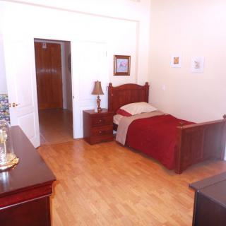 A cozy bedroom featuring a single bed with wooden furniture and minimalist decor.