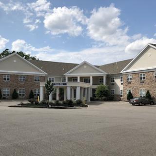 A well-maintained residential building featuring a classic exterior surrounded by landscaped gardens under a clear sky.