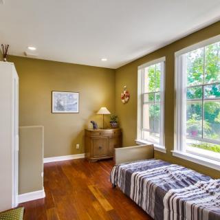 A cozy bedroom with a single bed, large windows, and warm decor.