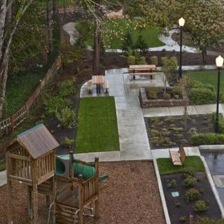 A scenic view of a park with a playground, benches, and lush greenery.