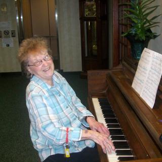 An elderly woman playing the piano with sheet music in front of her.