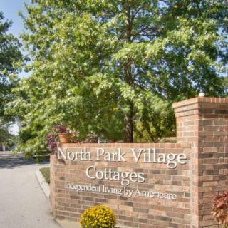 Entrance sign for North Park Village Cottages surrounded by trees and a roadway.
