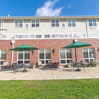 A building with a brick facade features outdoor seating with green umbrellas on a patio.