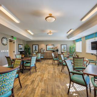 A well-lit dining area with multiple tables and chairs, featuring wooden flooring and decorative elements on the walls.