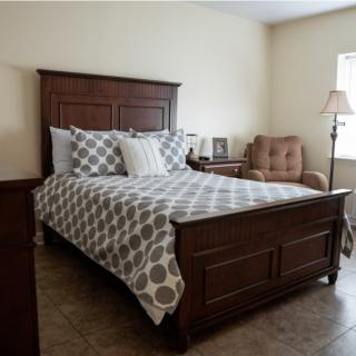 A cozy bedroom with a wooden bed, patterned bedding, and an armchair by the window.
