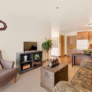 A cozy living room with a television, sofa, and armchair, connected to an open kitchen area.