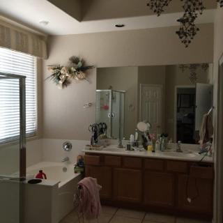 A spacious bathroom with a large mirror, bathtub, and sink, illuminated by natural light from a window.