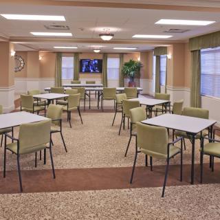 A spacious community dining room with several tables and chairs, featuring a television and large windows.